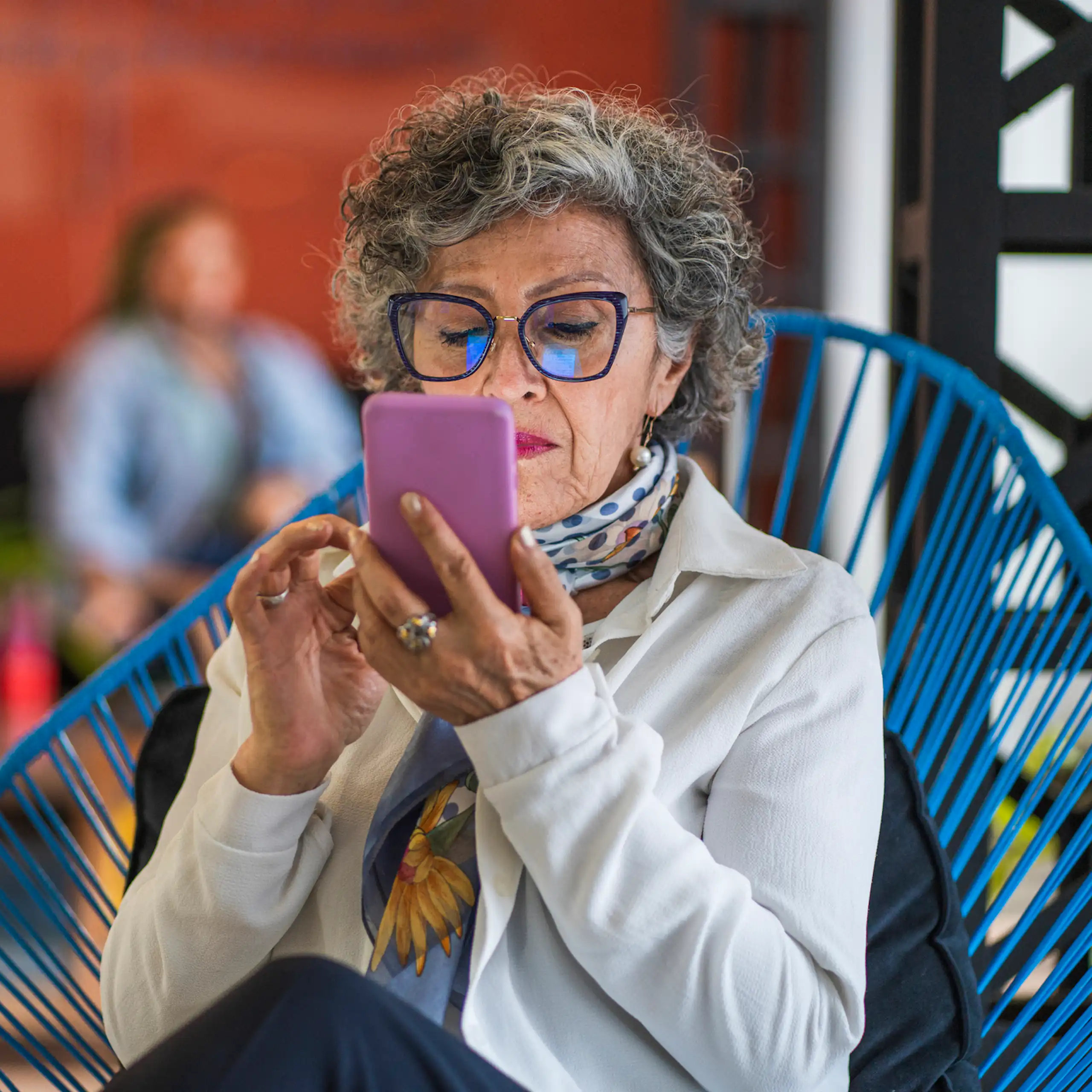 An older woman in a fabulous outfit reads something on her purple smartphone.