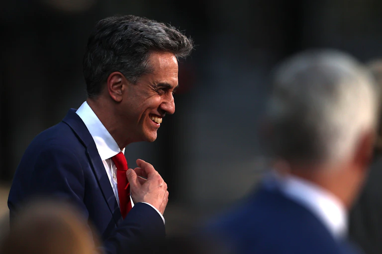 Close-up of a grinning Ed Miliband adjusting his tie