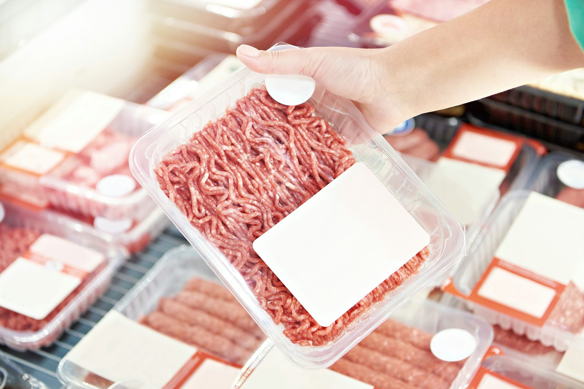 meat mince in plastic package, hand lifting packet from fridge of supermarket meats