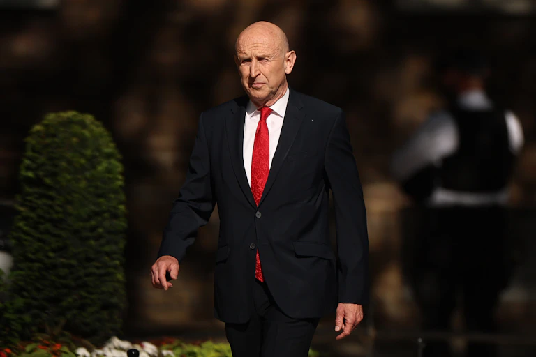 john healey in suit and red tie walking up downing street.
