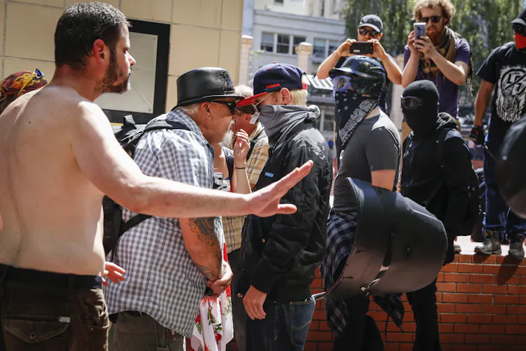A man with a bandana covering his face faces off against a man with a black hat.
