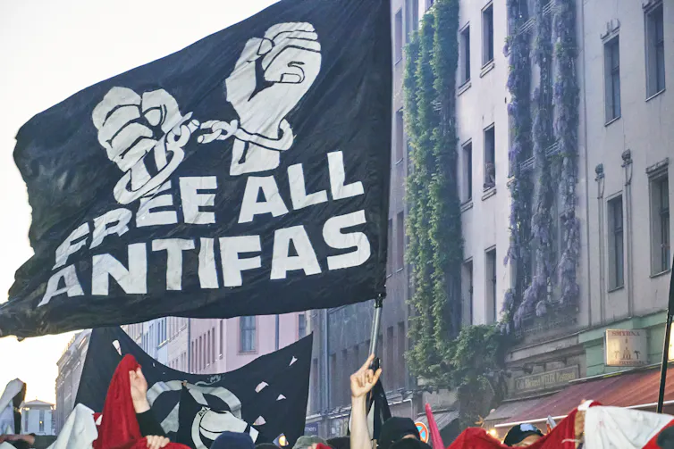 Protesters hold a black banner while walking on a city street.