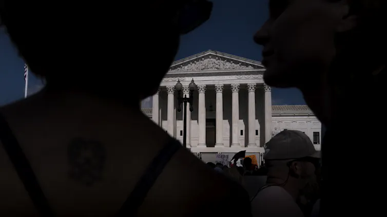 Several people stand in front of a federal building with columns.