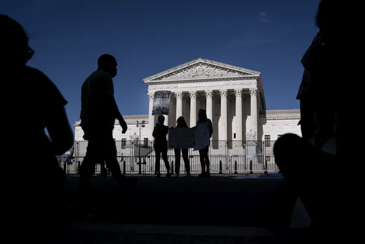 Several people gather in front of a federal building with columns.
