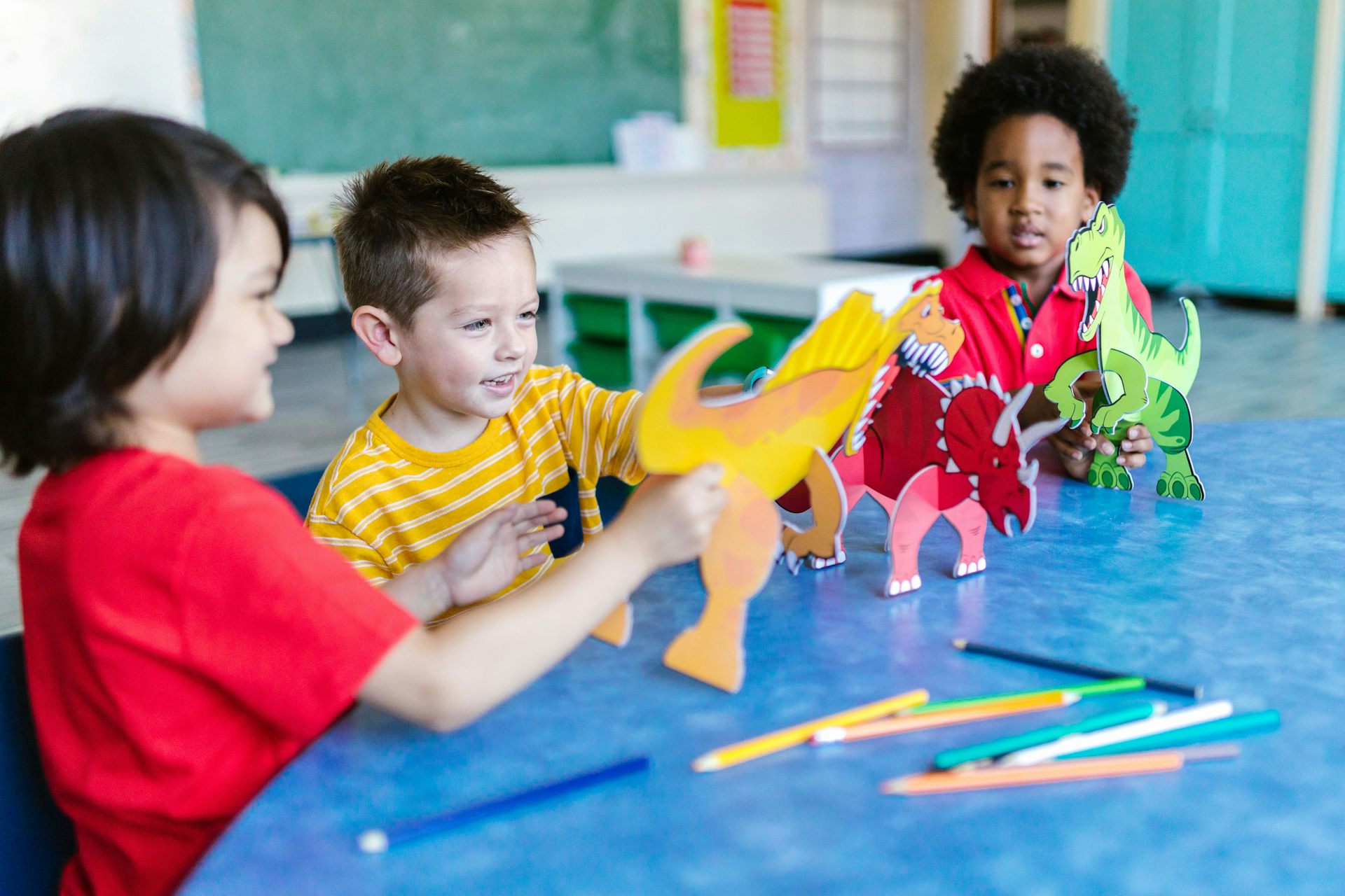 Children at a table holding dinosaur figures.
