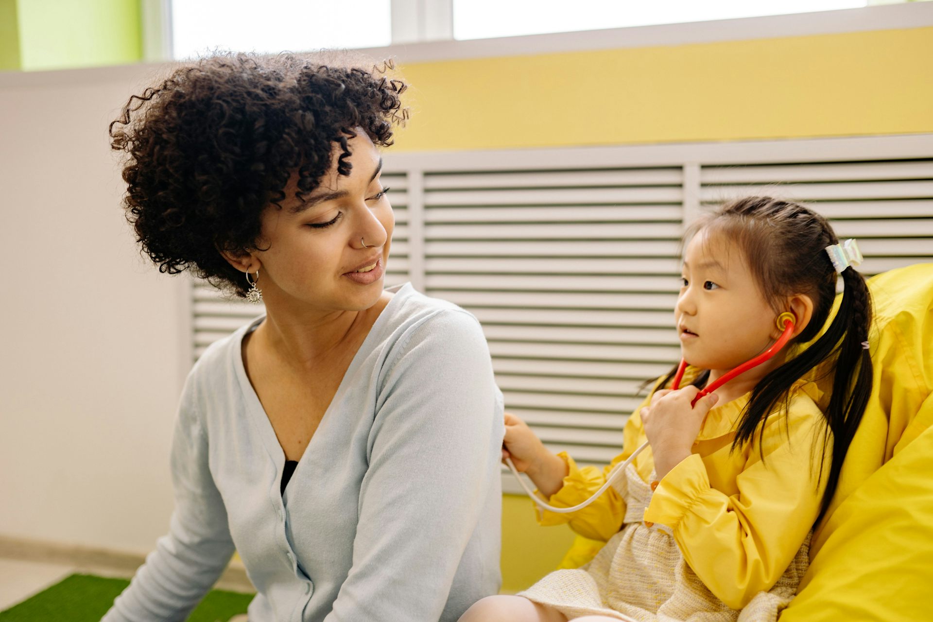 A child with a stethoscope plays doctor with a teacher.