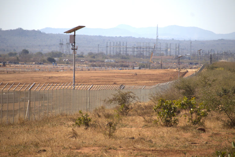 A large area of dry, brown grassland with a few shrubs and a high, reinforced fence cutting through it for about 2 kilometres.