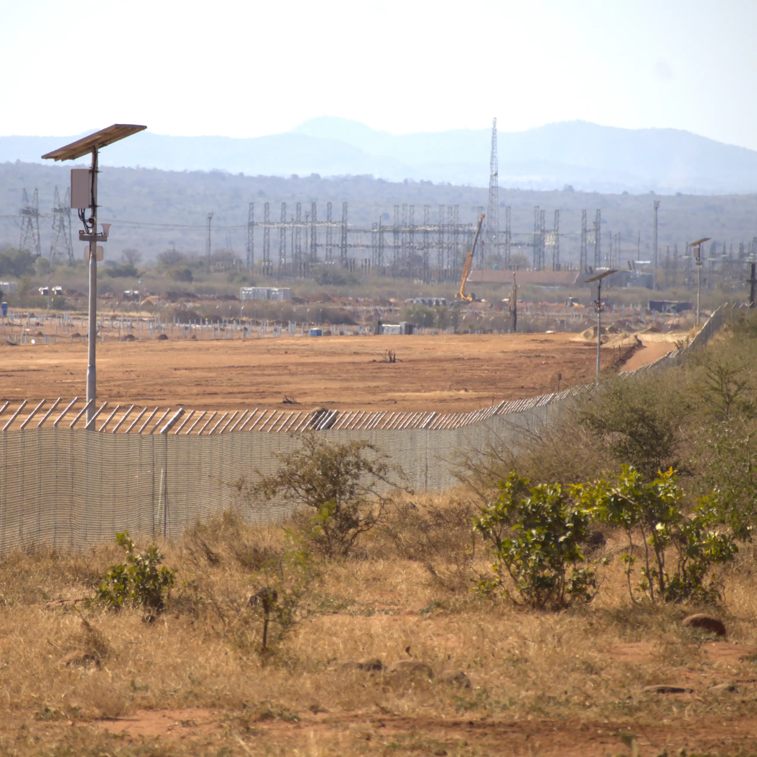 A large area of dry, brown grassland with a few shrubs and a high, reinforced fence cutting through it for about 2 kilometres.