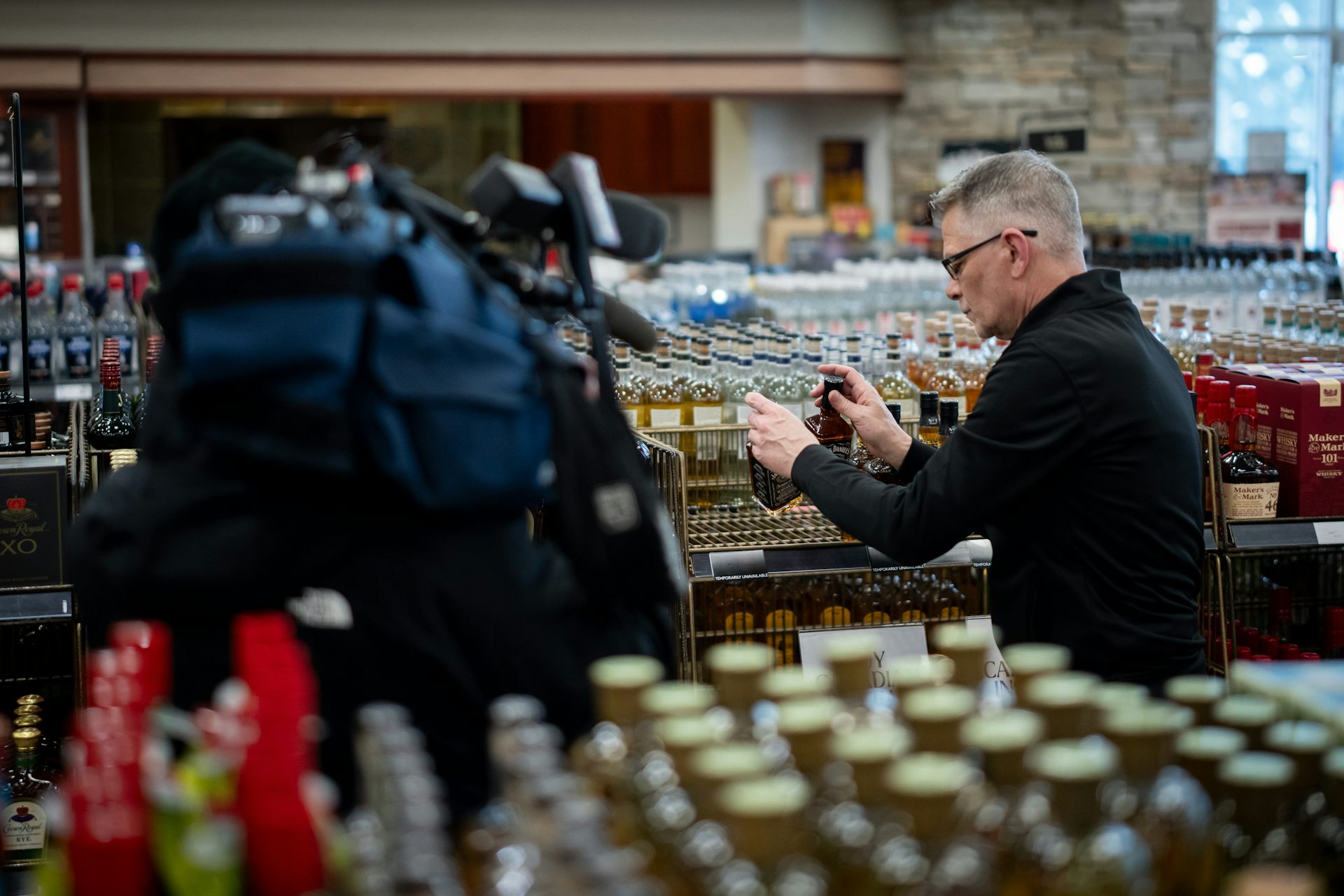 A man removes bottles of whiskey from a shelf in a liquor store
