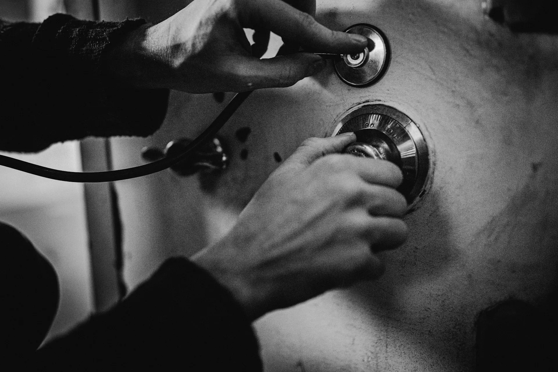 a person's left hand holds a stethoscope to a surface while the right hand turns a numbered dial