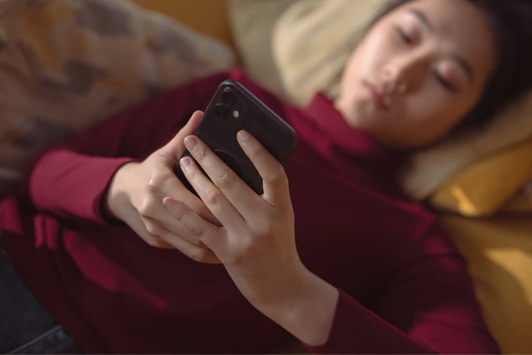 Uma jovem deitada, navegando no celular