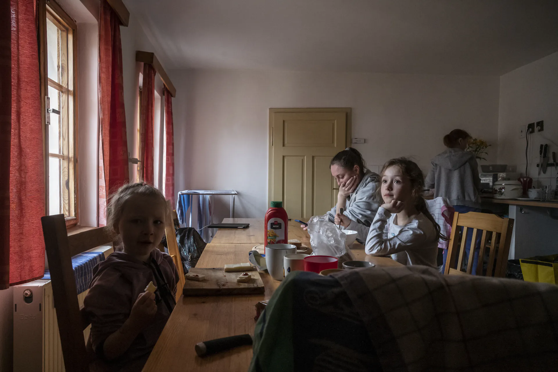 A glum family gathers at a dining table in a dimly lit room.