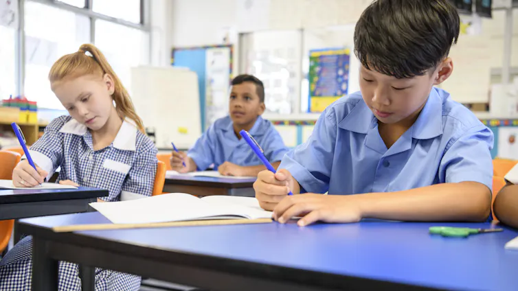 A young boy in a blue shirt with other pupils sitting in classroom doing their school work.