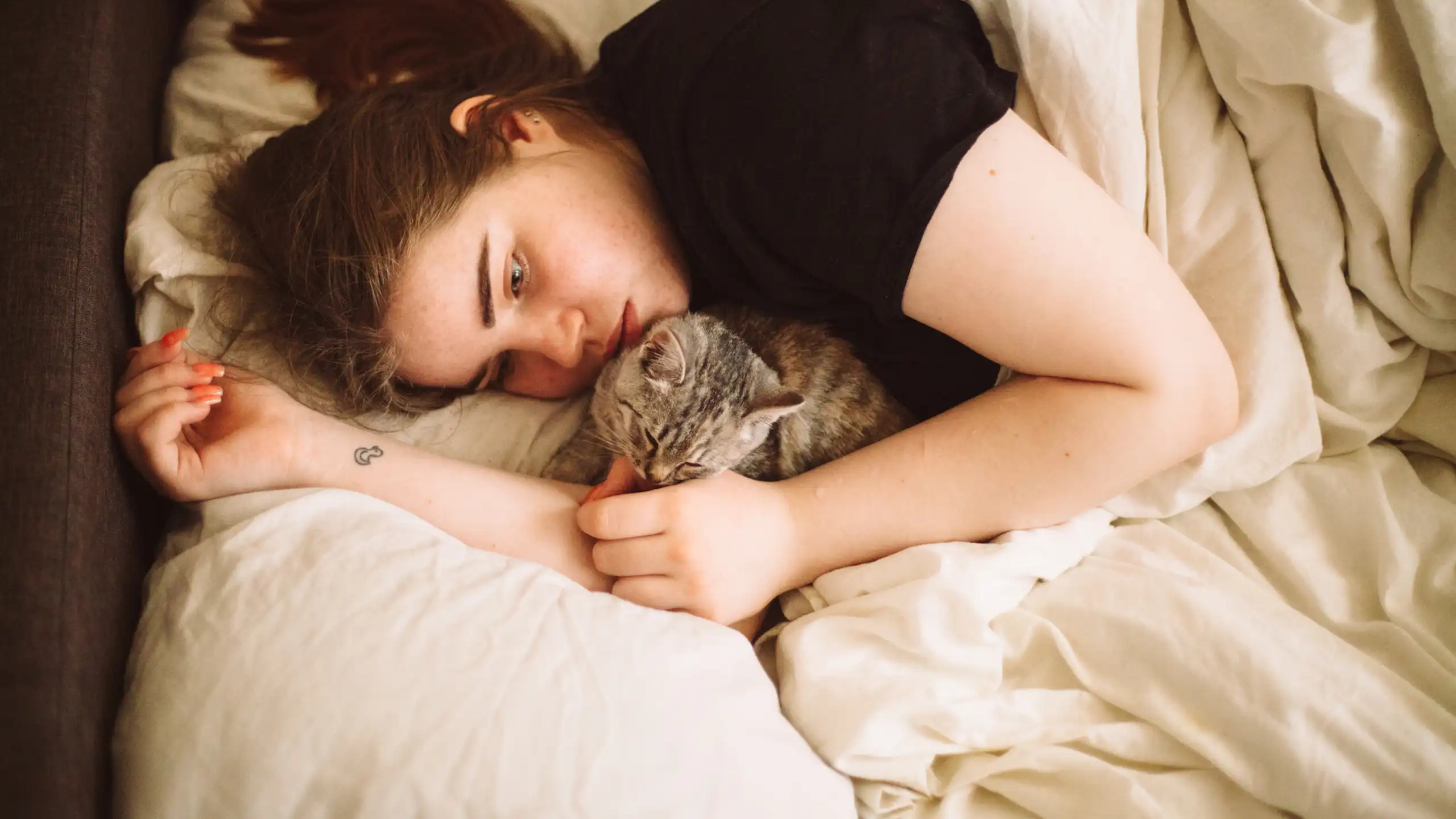 Teenage girl lying in bed, looking sad, with tabby cat