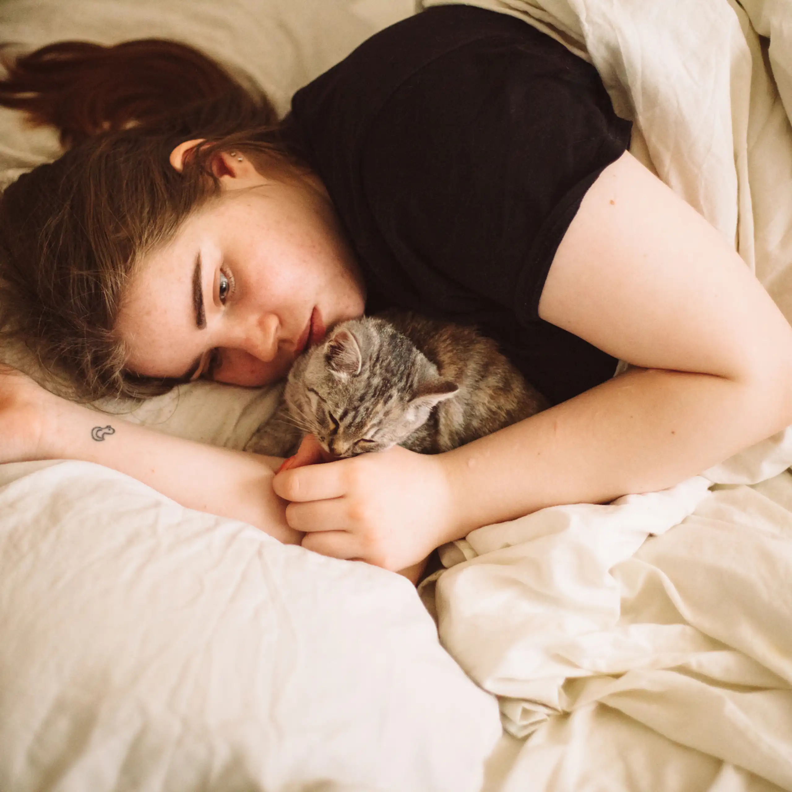 Teenage girl lying in bed, looking sad, with tabby cat