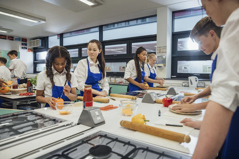 A low-angle view of a group of high school students working in pairs and small groups to make their own fresh pizza from scratch.
