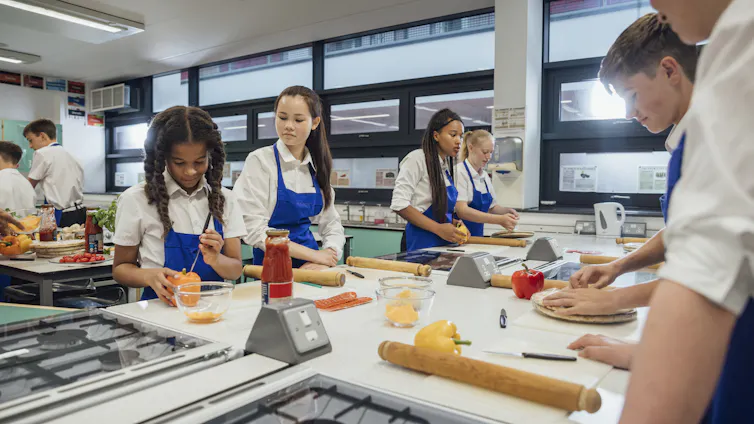 A low-angle view of a group of high school students working in pairs and small groups to make their own fresh pizza from scratch.