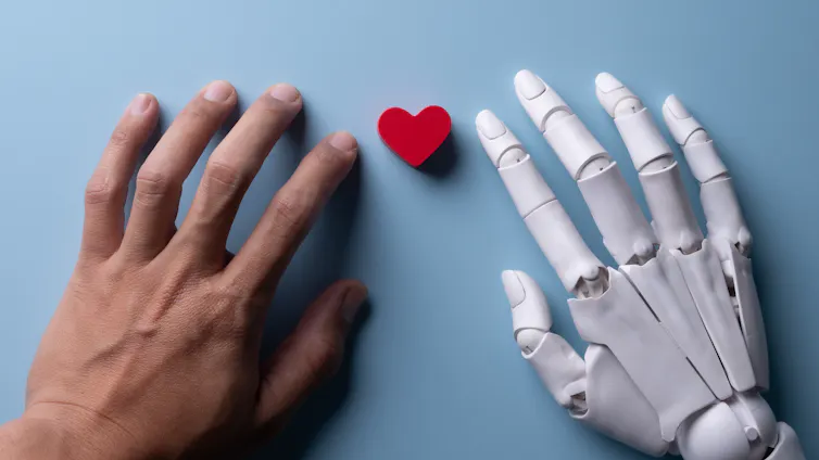 Una mano humana junto a otra robótica con un pequeño corazón en el centro