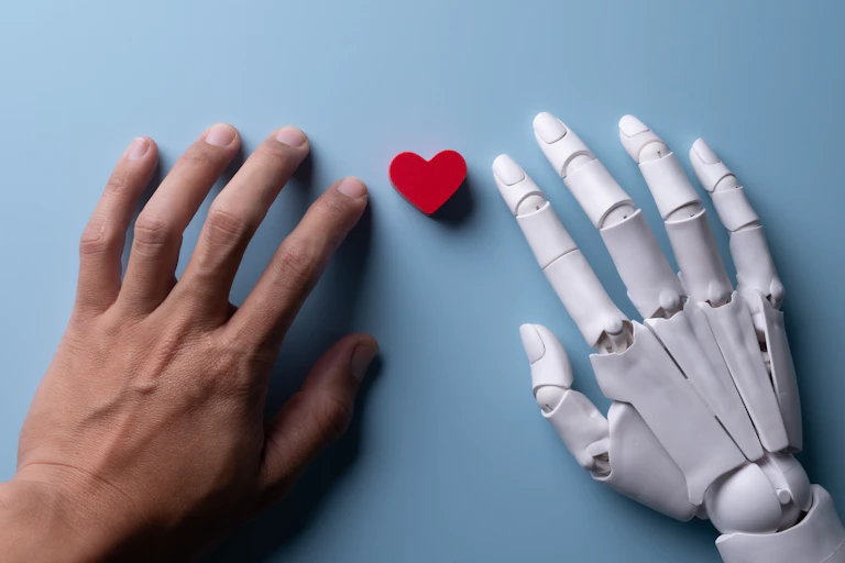 Una mano humana junto a otra robótica con un pequeño corazón en el centro