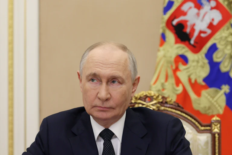 Head and shoulders shot of Vladimir Putin sitting at a desk with imperial Russian flag in the background.