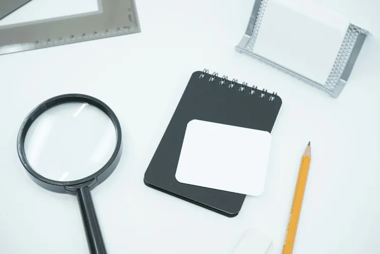 A magnifying glass next to a computer and notepad.