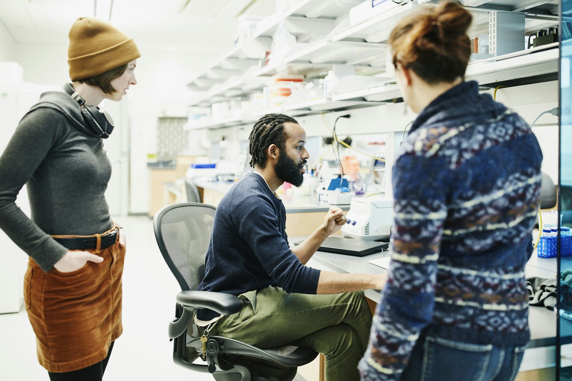 Tres personas en un laboratorio miran una computadora y hablan