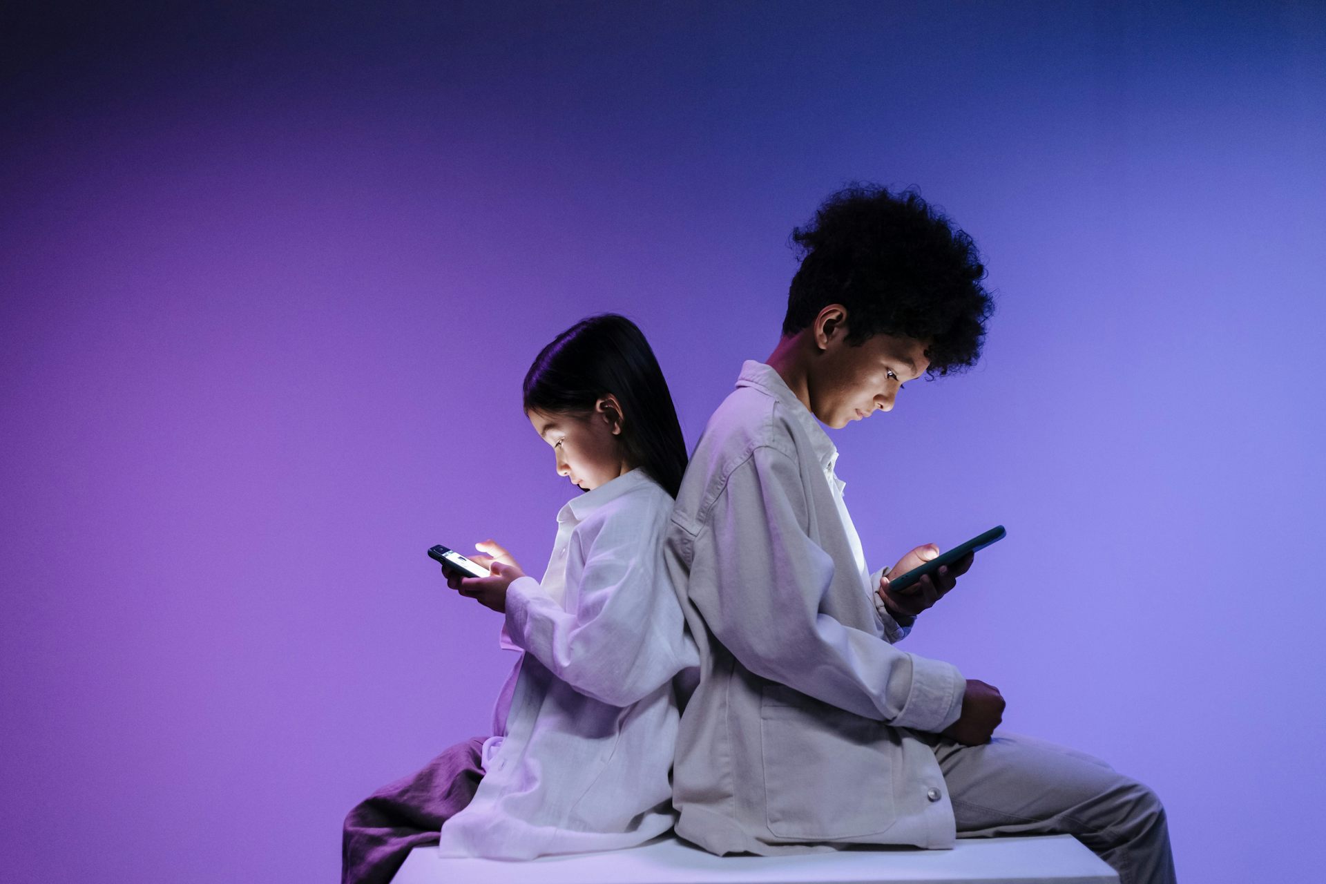 Two children back to back using smartphones on a vibrant purple background.