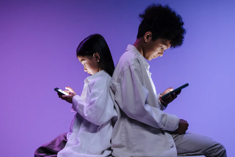 Two children back to back using smartphones on a vibrant purple background.