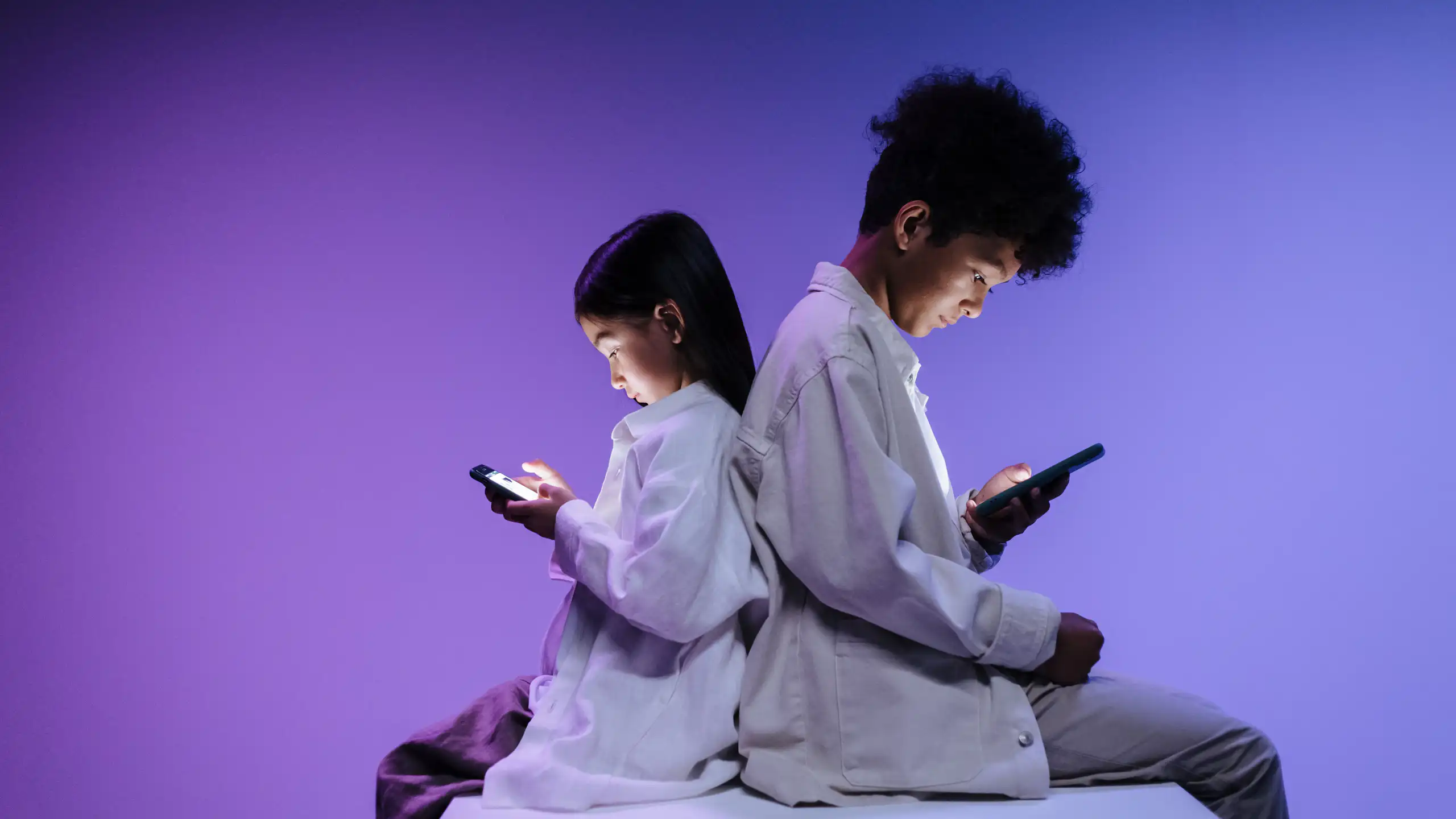 Two children back to back using smartphones on a vibrant purple background.