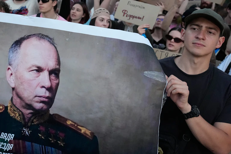 Protesters in a city square hold up a portrait of a military commander.