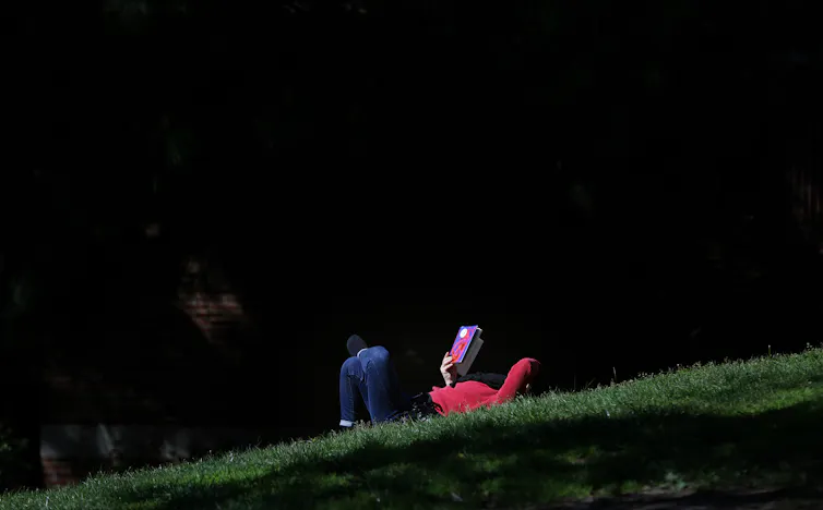 Una persona yace en la hierba con un libro en la cara bajo un oscuro cielo nocturno.