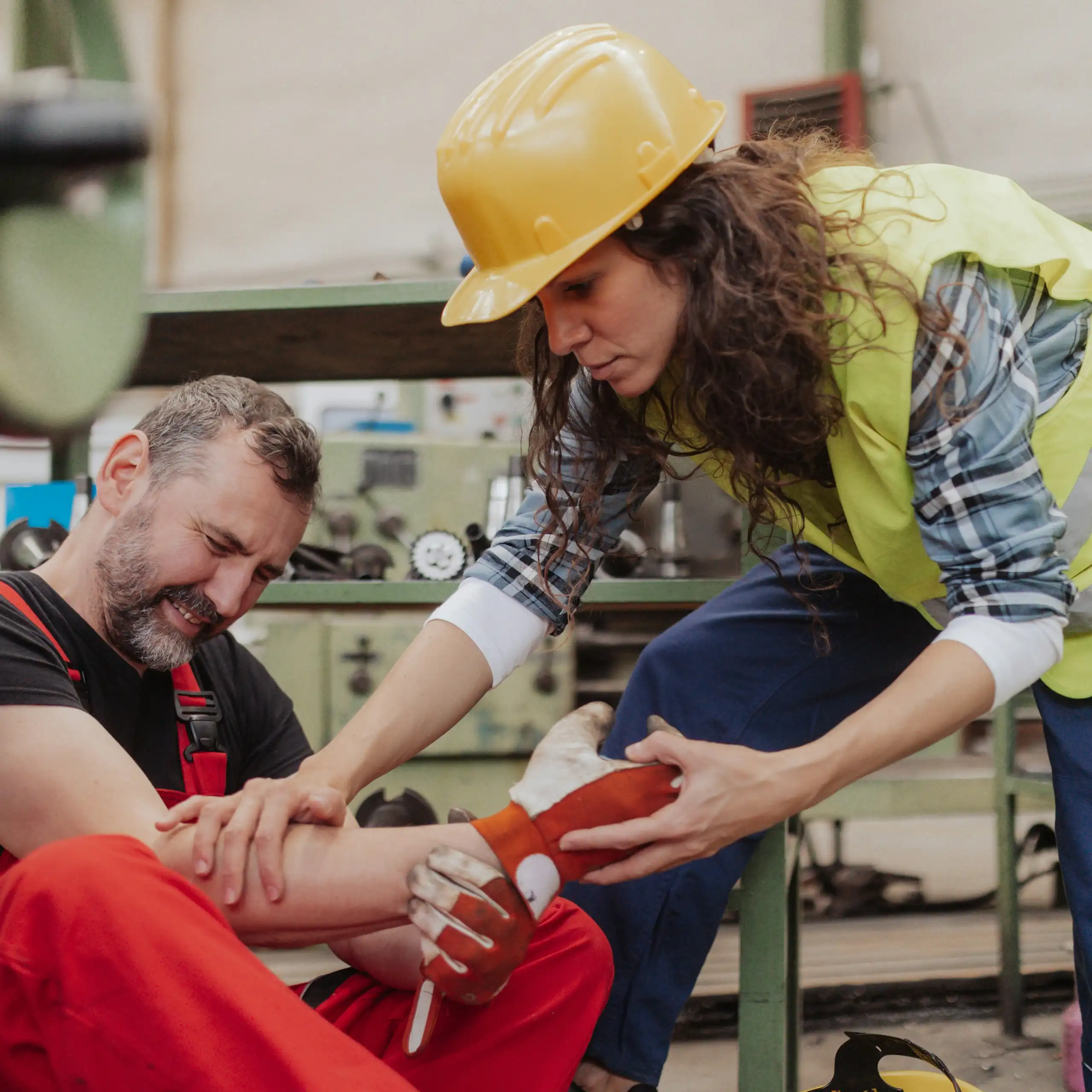 A woman in a hard hat offerss help to a man sitting on the ground, grimacing in pain