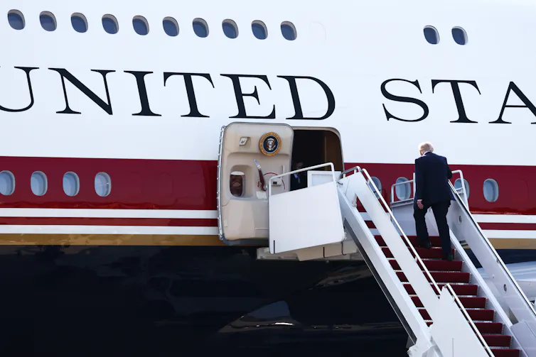 A man in a dark suit climbs a stairway to a large plane.