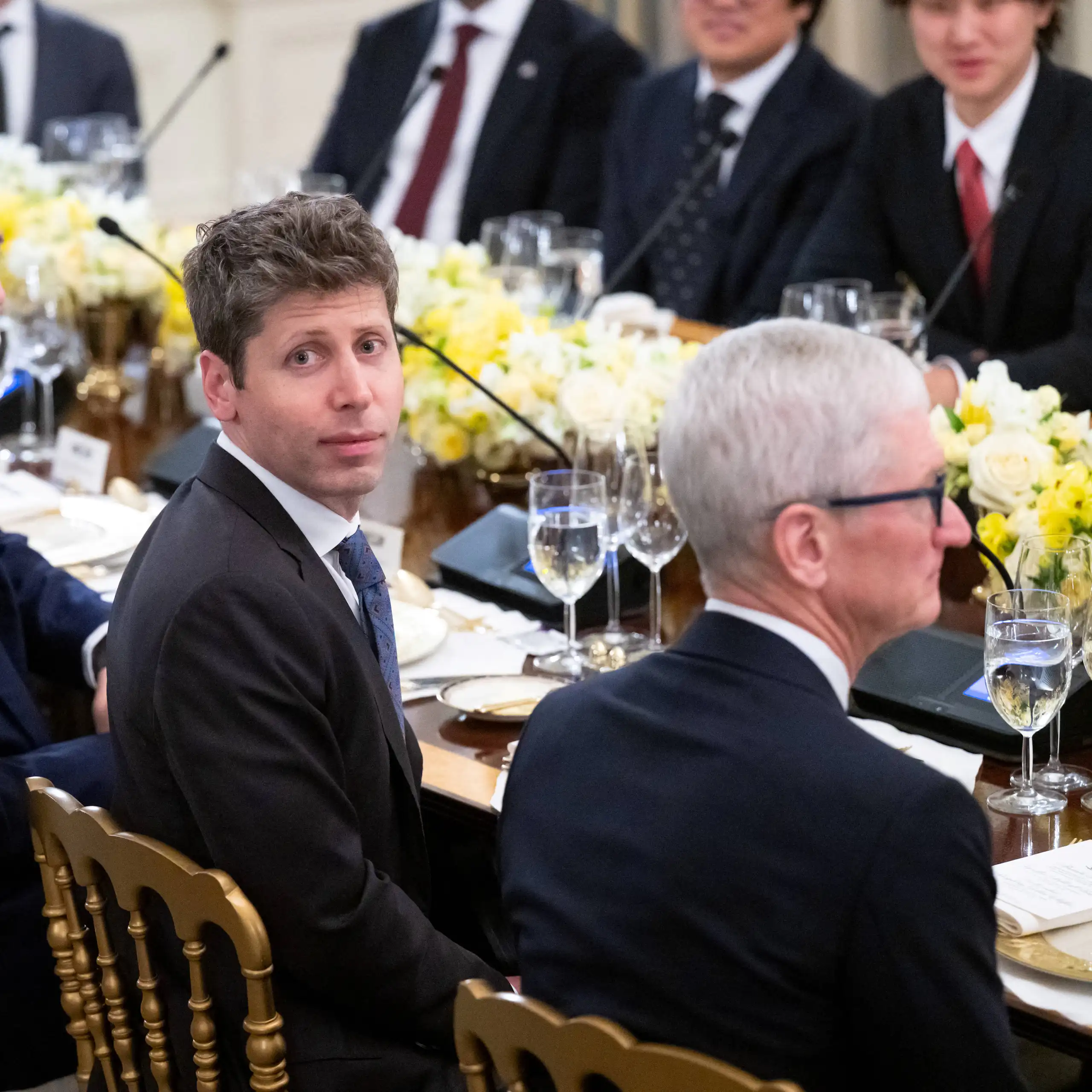OpenAI CEO Sam Altman and Apple CEO Tim Cook sitting next to each other at a table