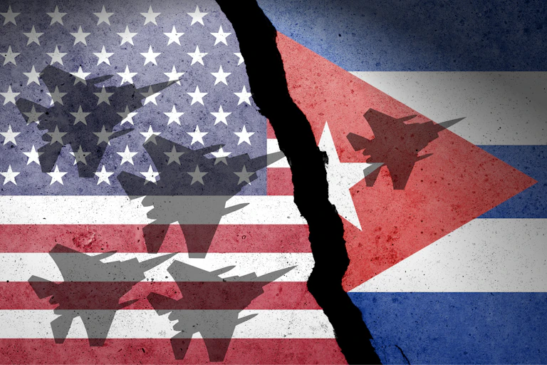 Bandera de Estados Unidos y de Cuba separadas por una brecha con sombras de aviones de combate sobre ellas