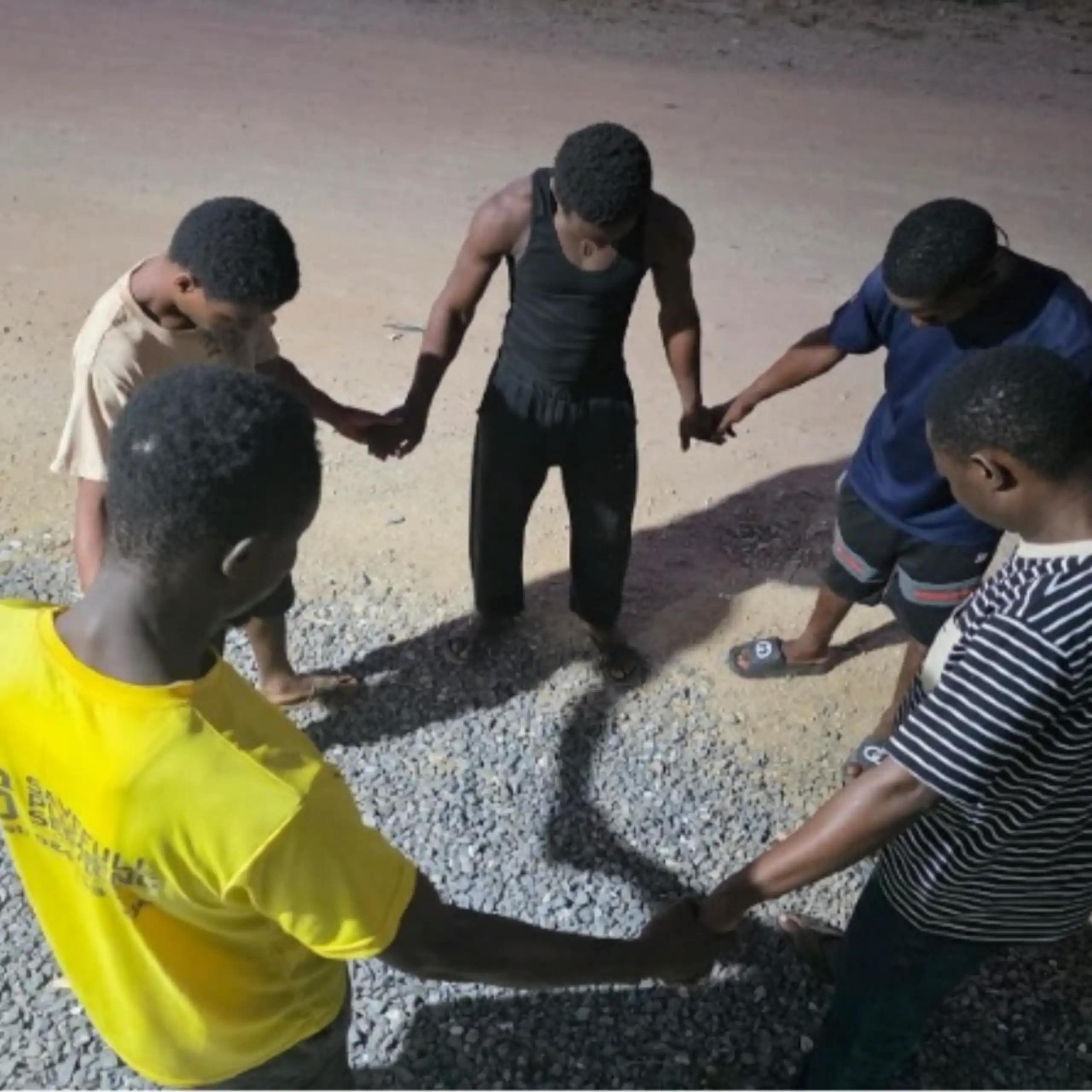 Young males stand in a circle, holding hands, with heads bowed