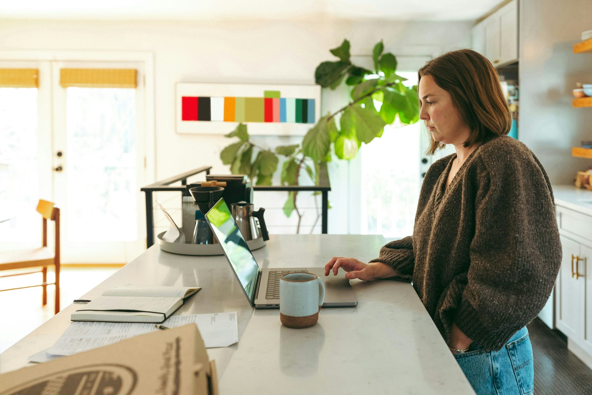 Une femme travaille devant son ordinateur, debout dans sa cuisine