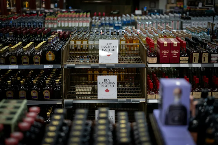 Des rayons vides dans un magasin d’alcool, sur lesquels sont accrochées des affiches indiquant « Achetez plutôt des produits canadiens »