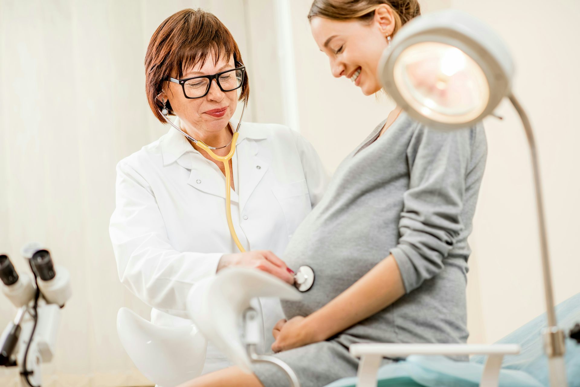 A pregnant woman with a doctor holding a stethoscope to her abdomen