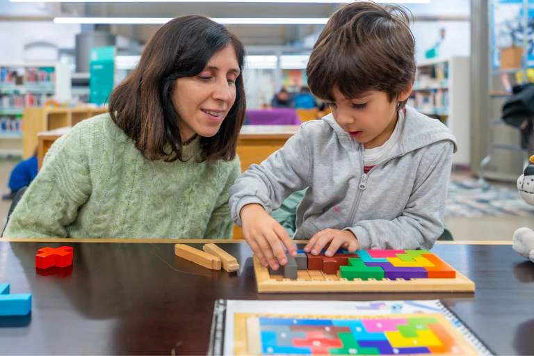 A mother watches her son play with a puzzle