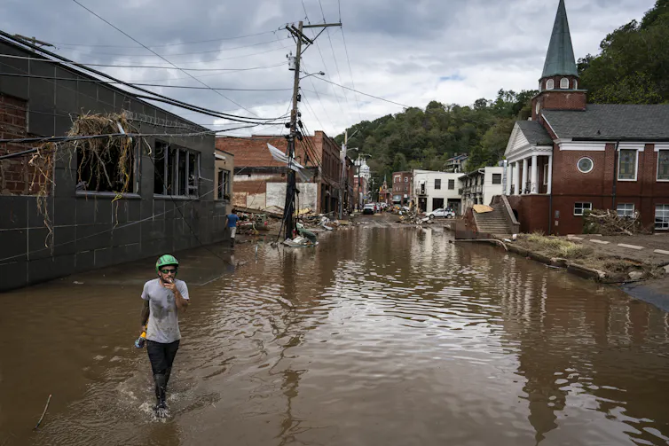 Una persona camina por una calle inundada detrás de la cual hay edificios dañados, incluida una iglesia.