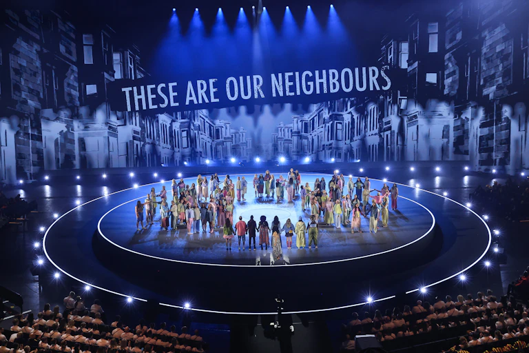 General view during the live performances of the Opening Ceremony of the Glasgow 2026 Commonwealth Games, with performers onstage and the text 'these are our neighbours' in the background.
