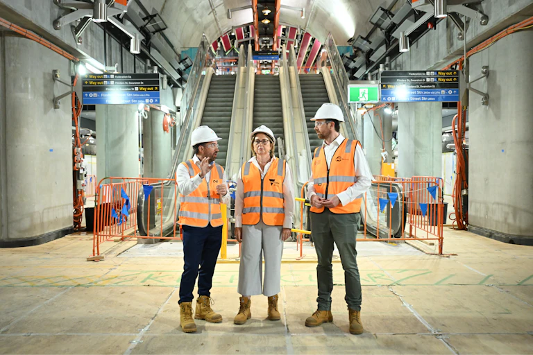Three politicians in high vis vests and hard hats stand inside a tunnel under construction