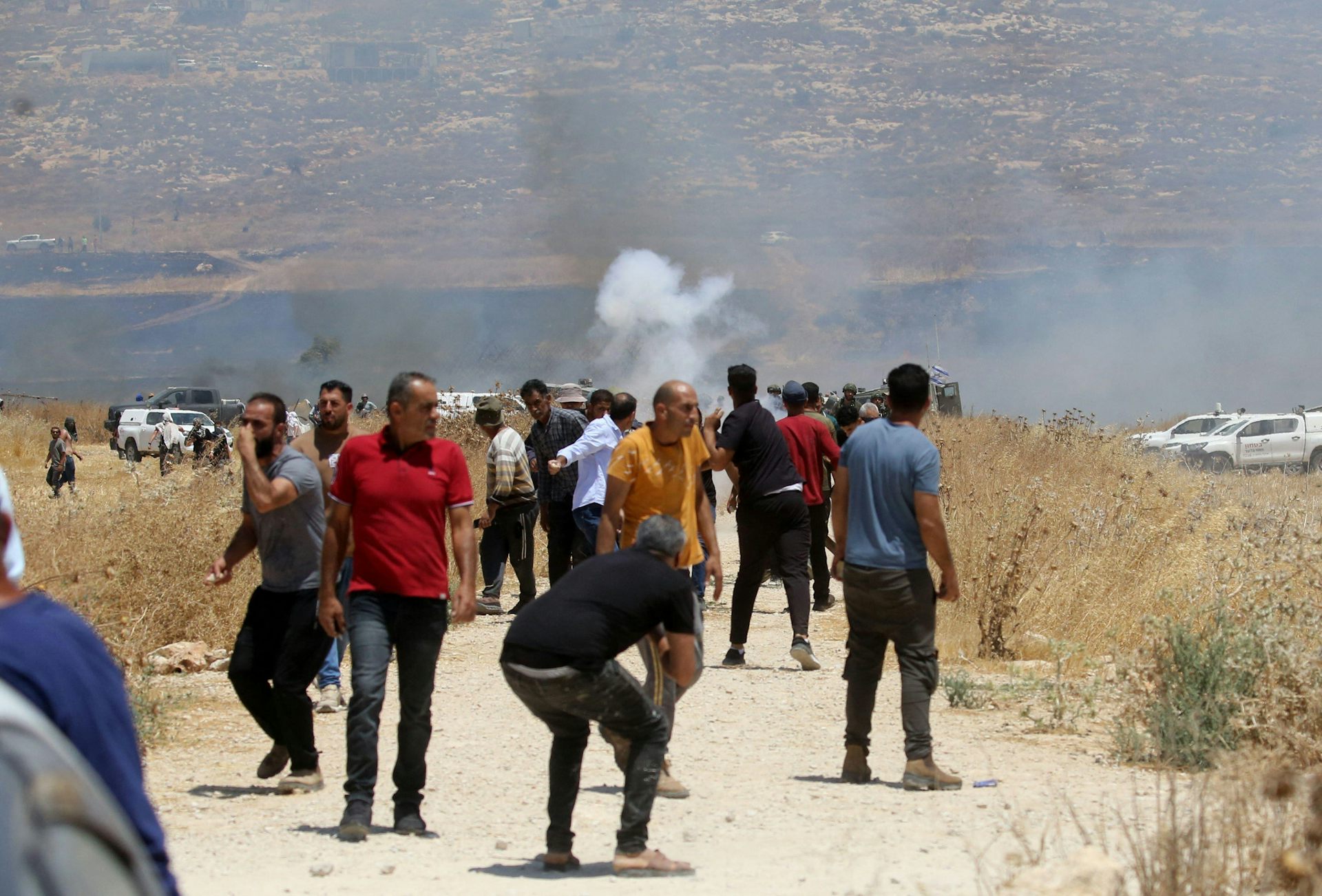Israeli men walk towards a fire. Security forces and trucks are in the background.