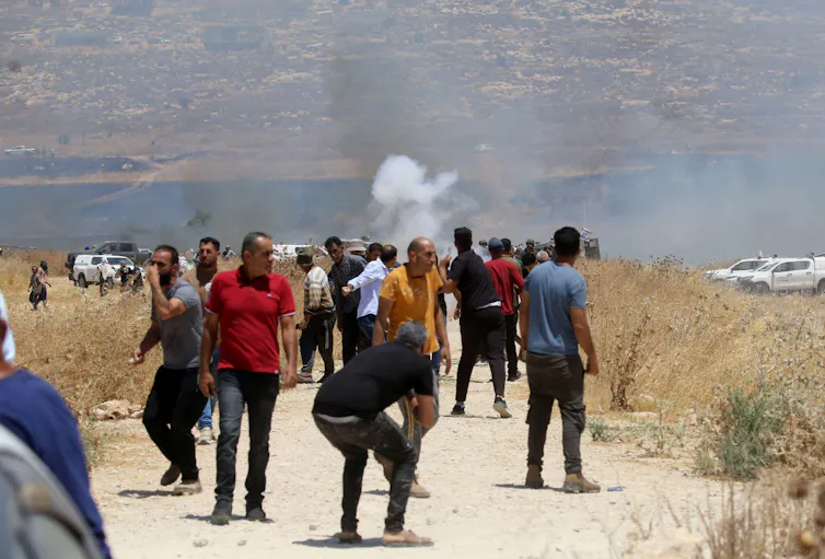 Israeli men walk towards a fire. Security forces and trucks are in the background.