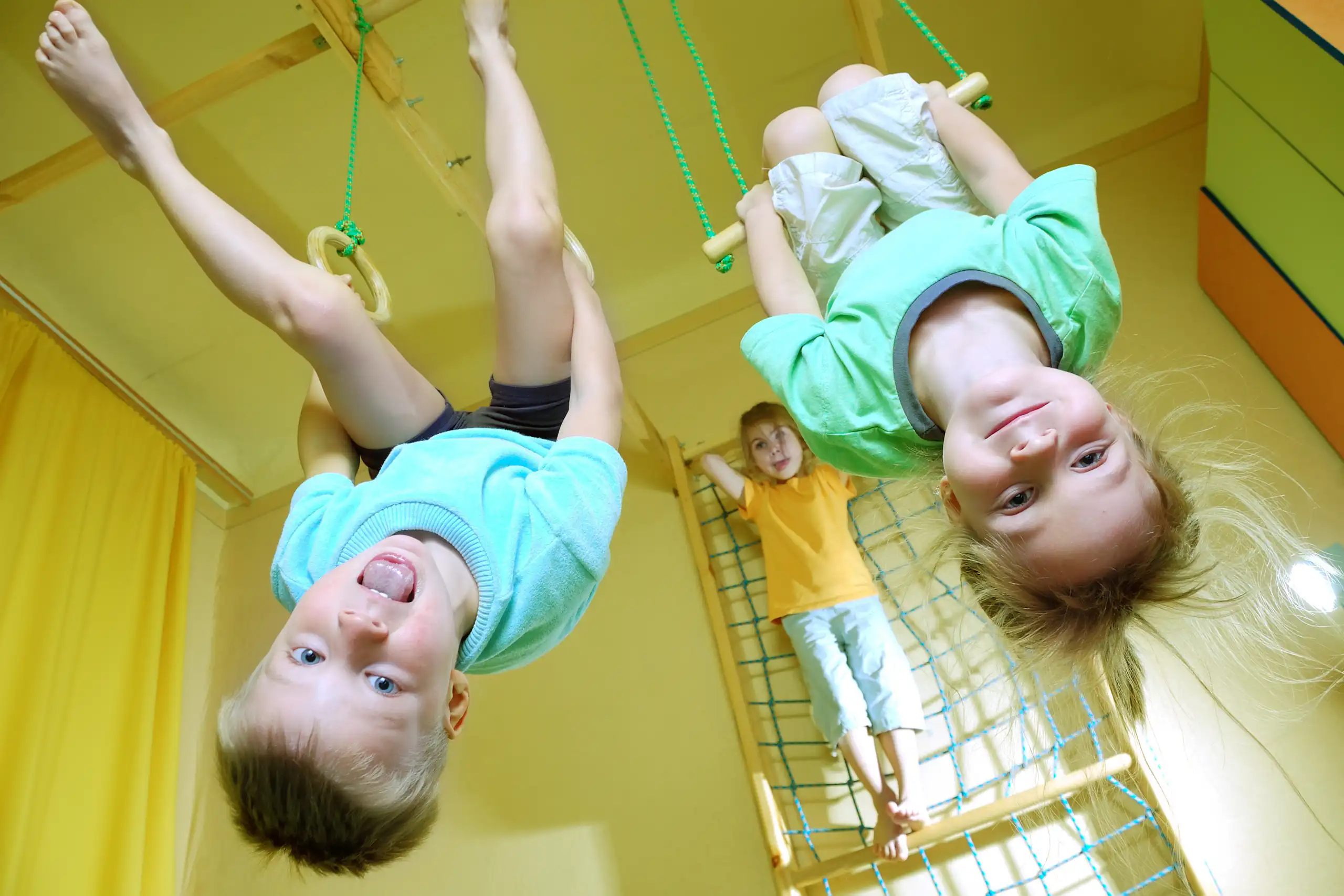 Dos niños colgados de un trapecio y unas anilllas, respectivamente, en primer plano