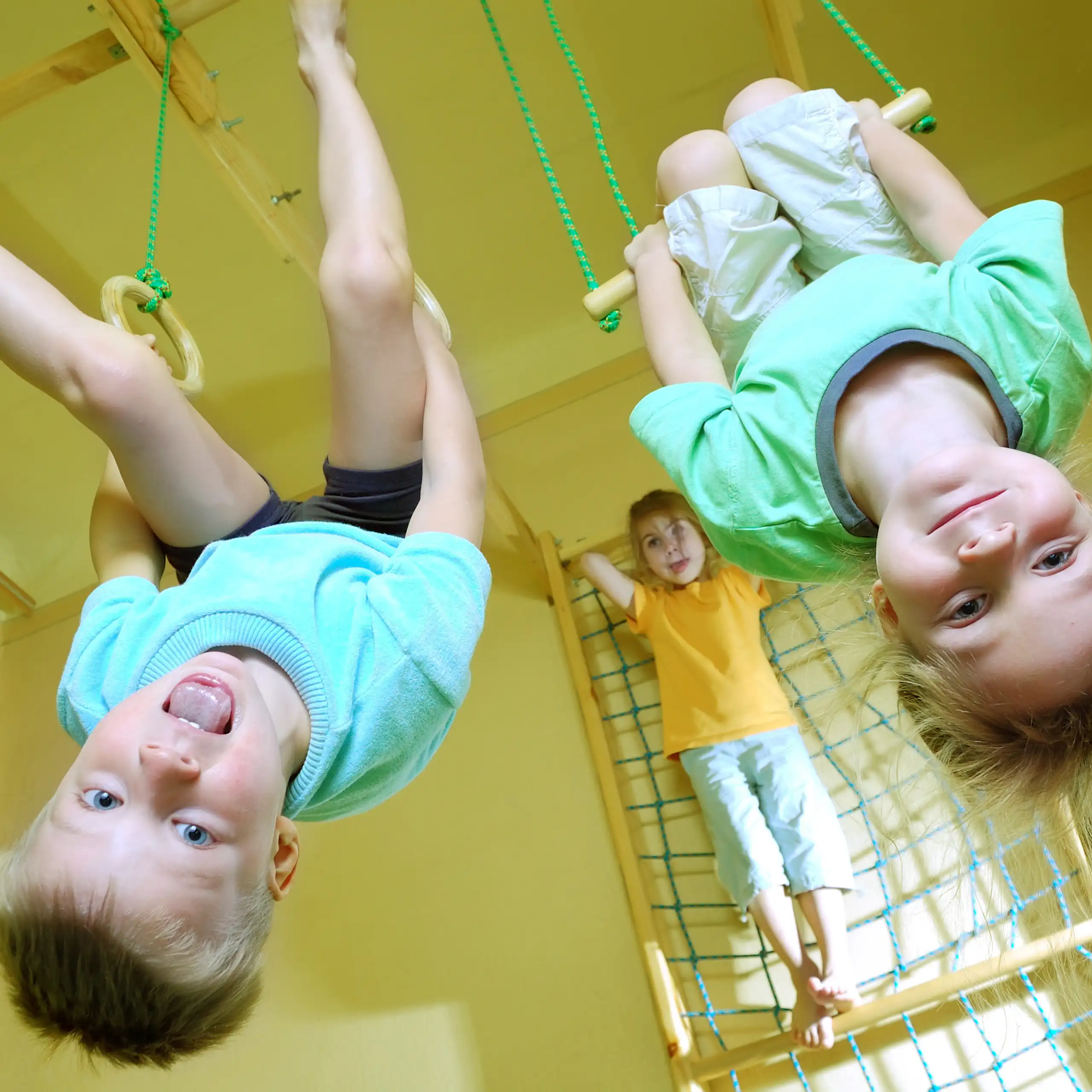 Dos niños colgados de un trapecio y unas anilllas, respectivamente, en primer plano