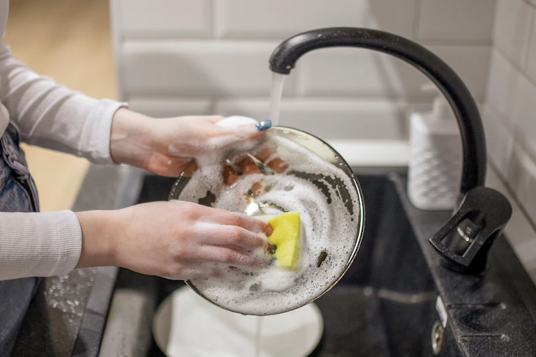 A person using a sponge to wash a plate in the kitchen sink.