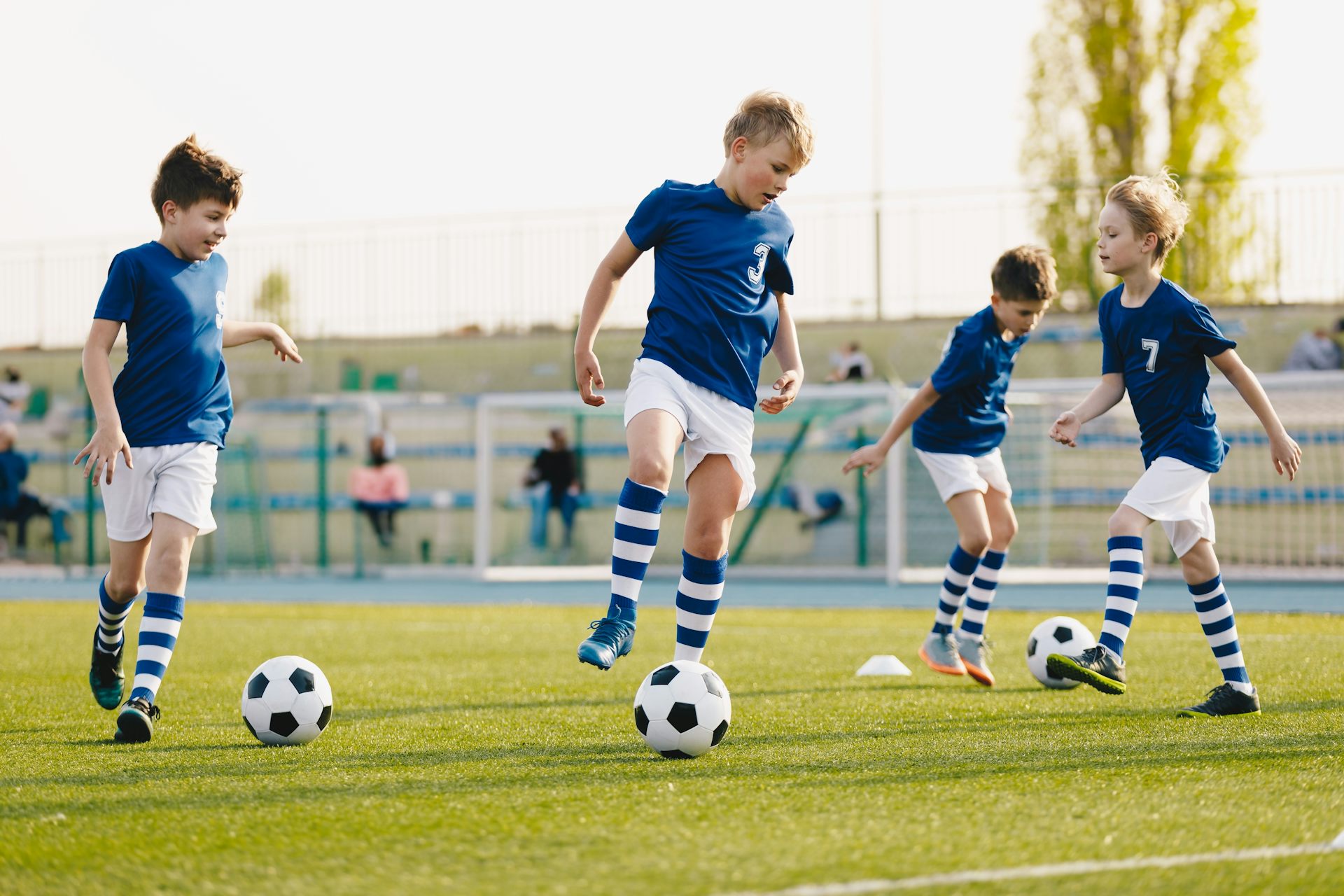 Un grup de nens vestits de blau i blanc juguen a un camp de gespa amb balons de futbol.