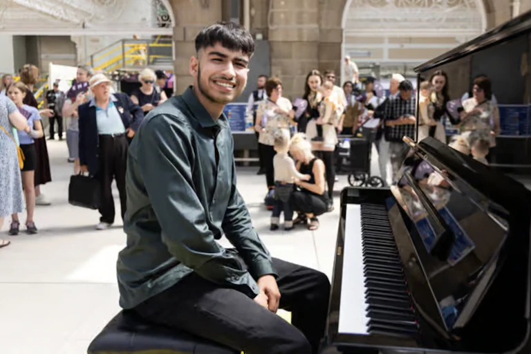 A young boy seated at a piano smiling.